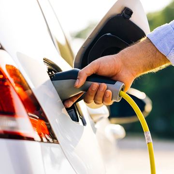 Person oplader elbil med et stik ved en ladestation.