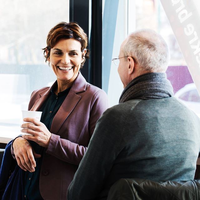 En kvinde og en mand nyder en samtale over kaffe i et lyst caféområde.